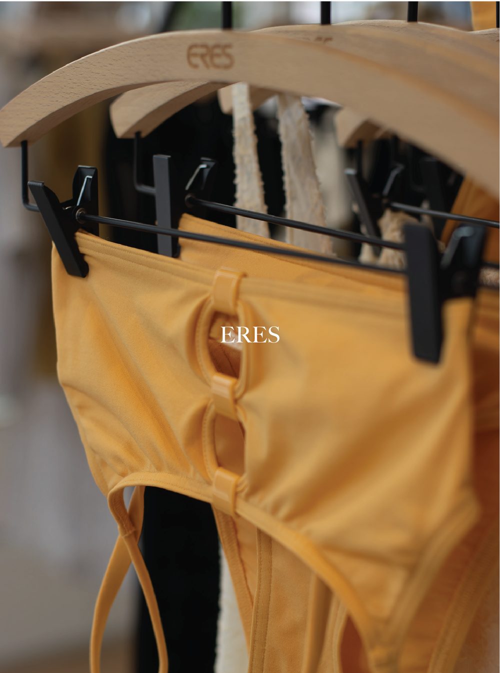 Yellow clothing item hanging on a hanger with black clips, underneath a wooden hanger with the word 'ERES' engraved on it. ERES.