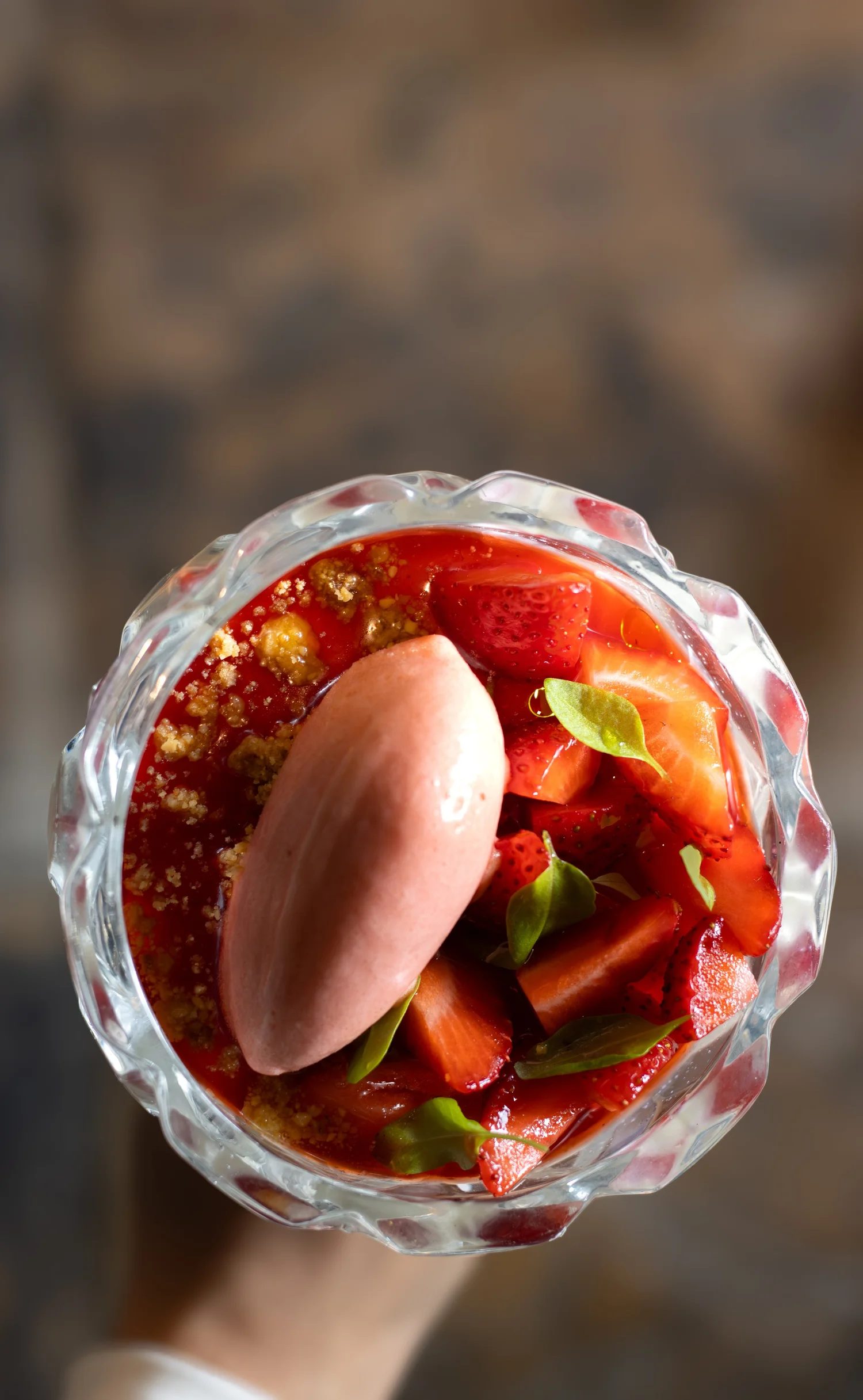 Top-down view of a glass bowl filled with sliced strawberries, garnished with small green leaves, with a dollop of pink sorbet and strawberry syrup on top. The Lamb Inn.