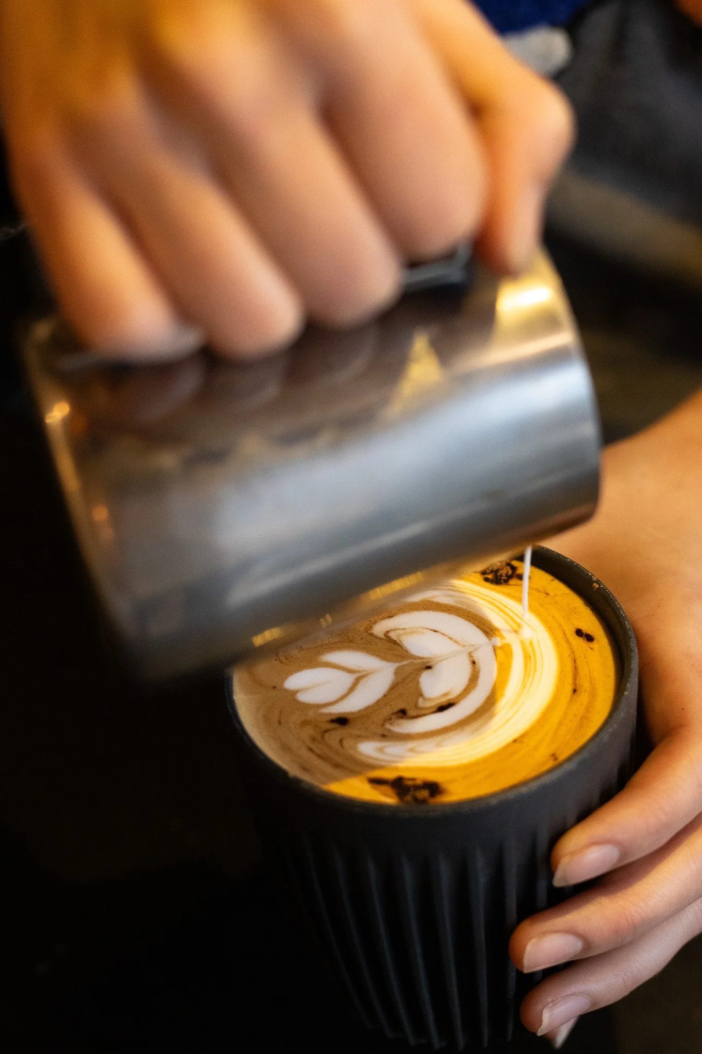 Person holding a milk frother over a cup of coffee with latte art in a coffee shop. The Scandinavian Coffee Pod.