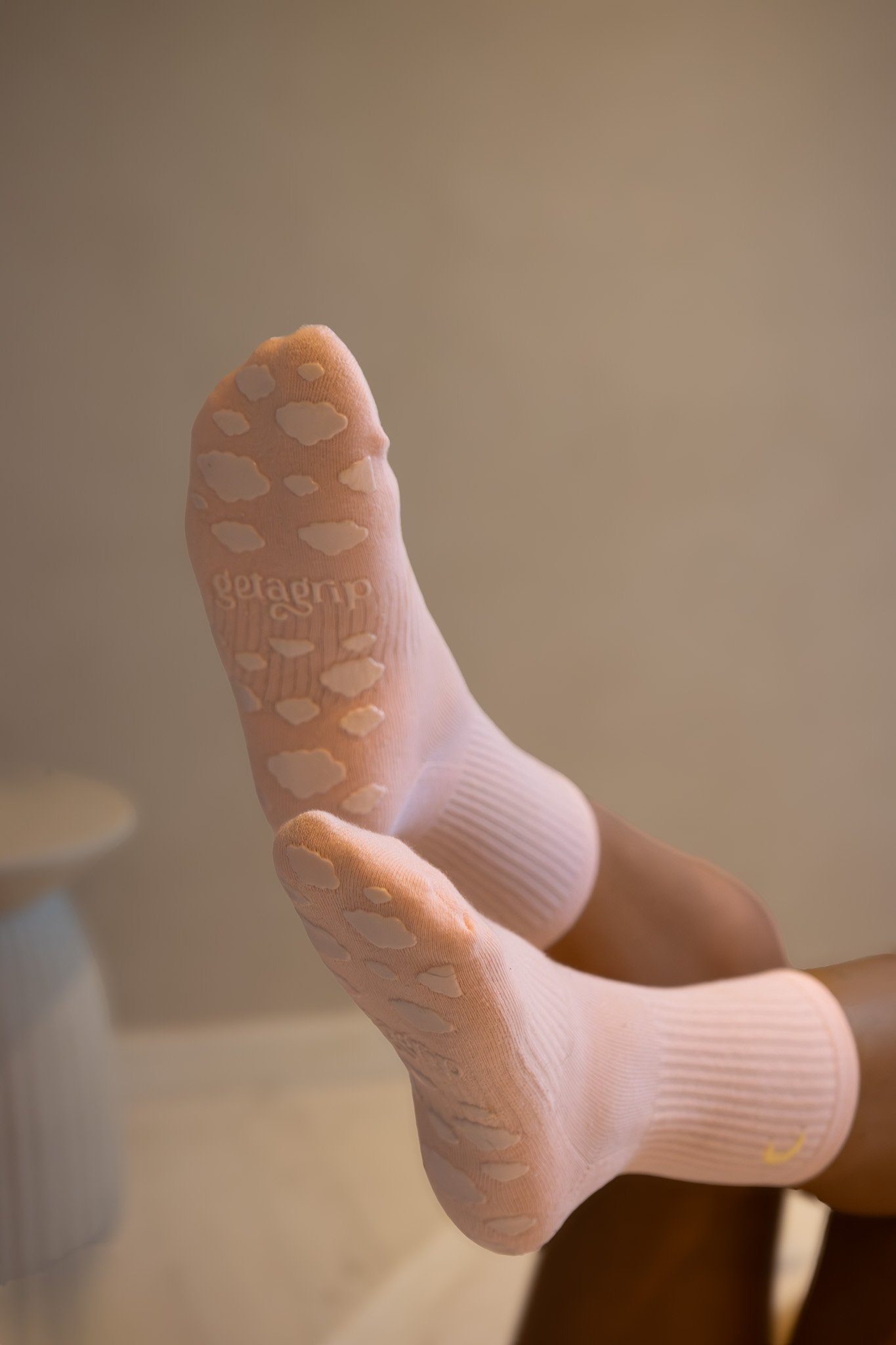 A close-up of a person's foot wearing a light pink sock with white cloud patterns, with the heel in focus and a plain background. Shona Manderson, Get A Grip.