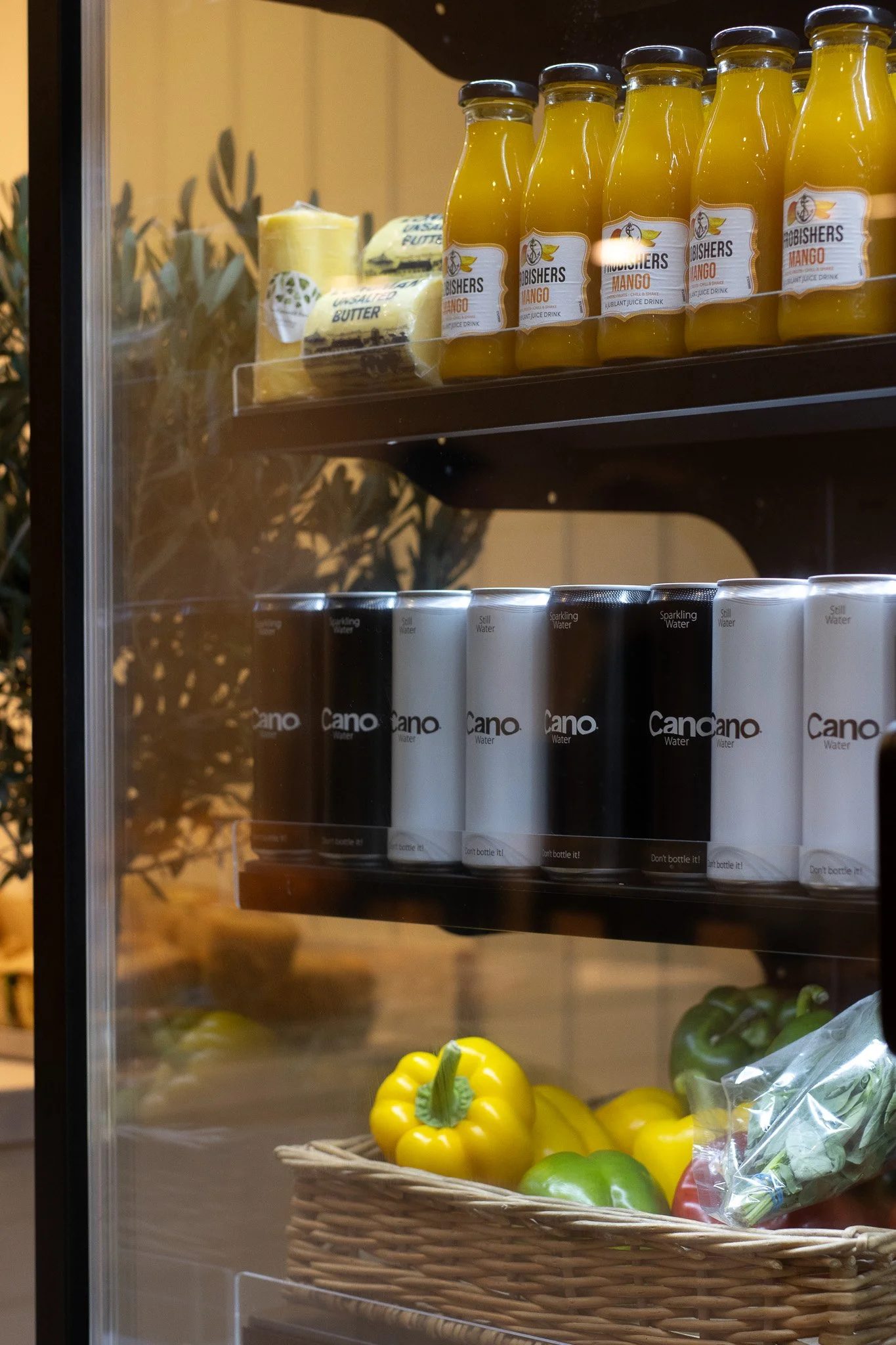 Refrigerator door with bottles of Mango juice, blocks of butter, and a basket of yellow and green bell peppers and other vegetables. The Cotswold Farm.