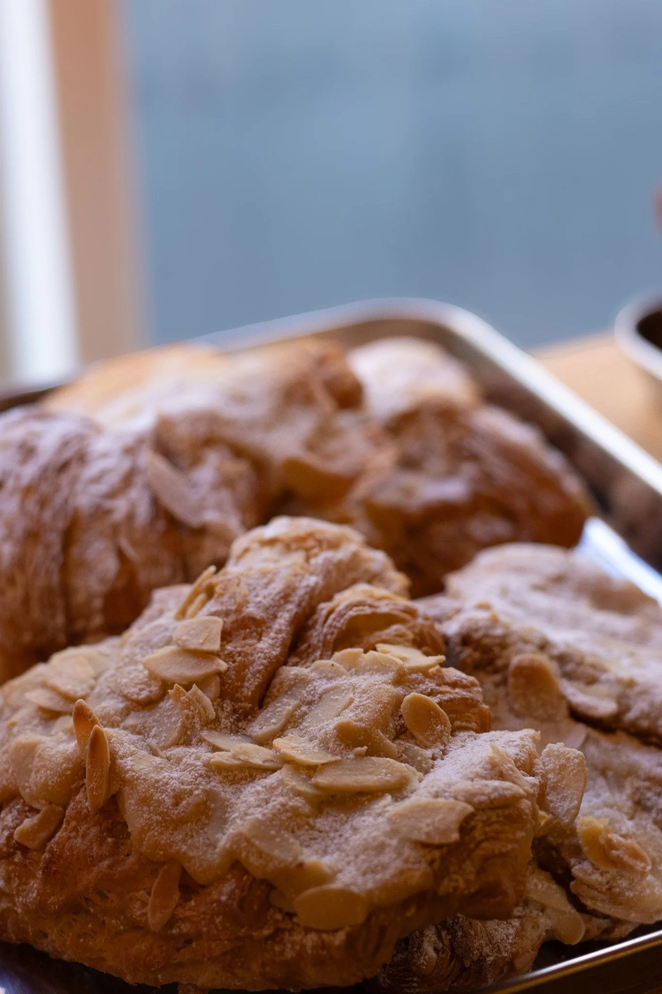 Close-up view of an almond pastry with sliced almonds on top, dusted with powdered sugar, on a baking sheet. The New England Coffee House.