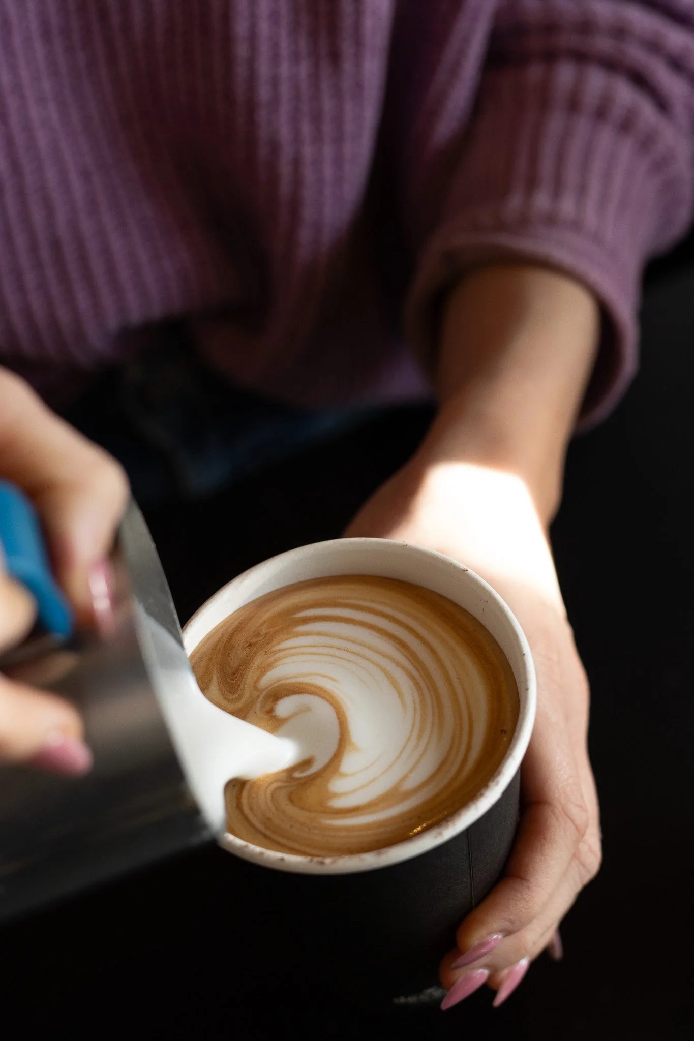 Close-up of a person pouring steamed milk into a cup of espresso, creating latte art with a swirl pattern. The Scandinavian Coffee Pod.