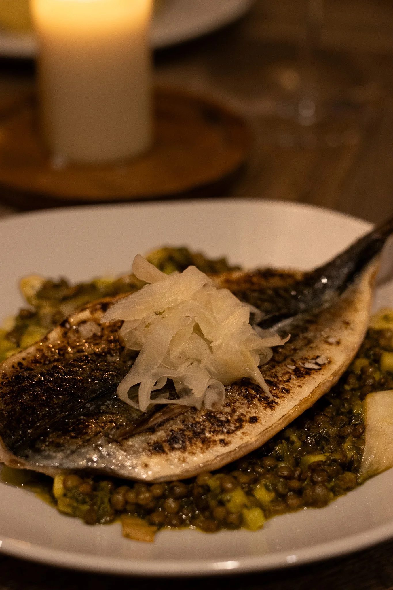 A plate of grilled fish garnished with shredded white onion, served on a bed of green lentils or split peas with herbs. The Lamb Inn.