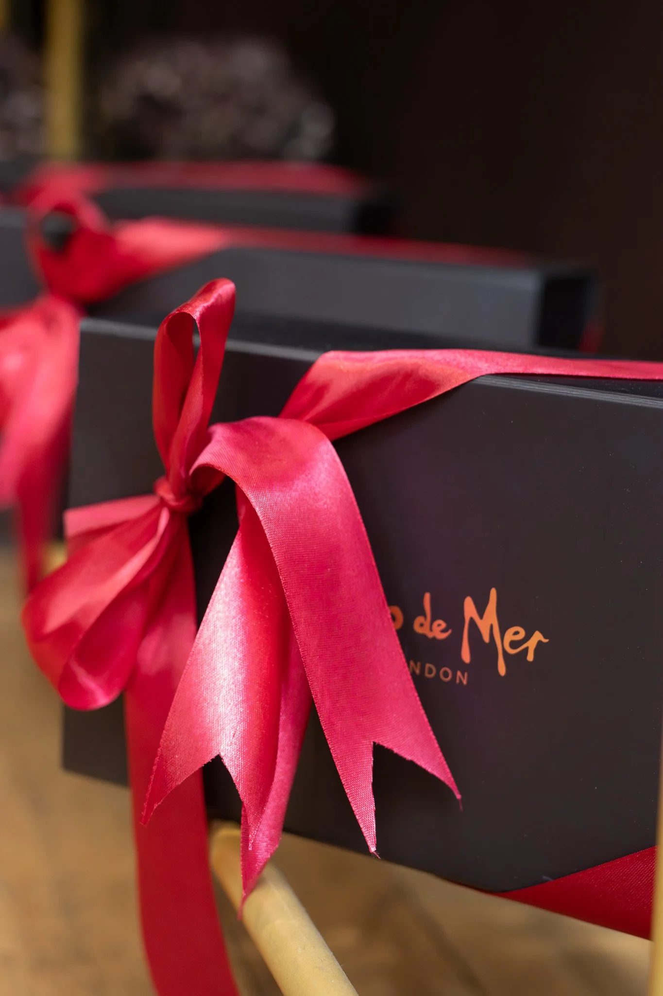 Close-up of a black gift box with orange writing, decorated with a pink satin ribbon tied into a bow. Coco De Mer.