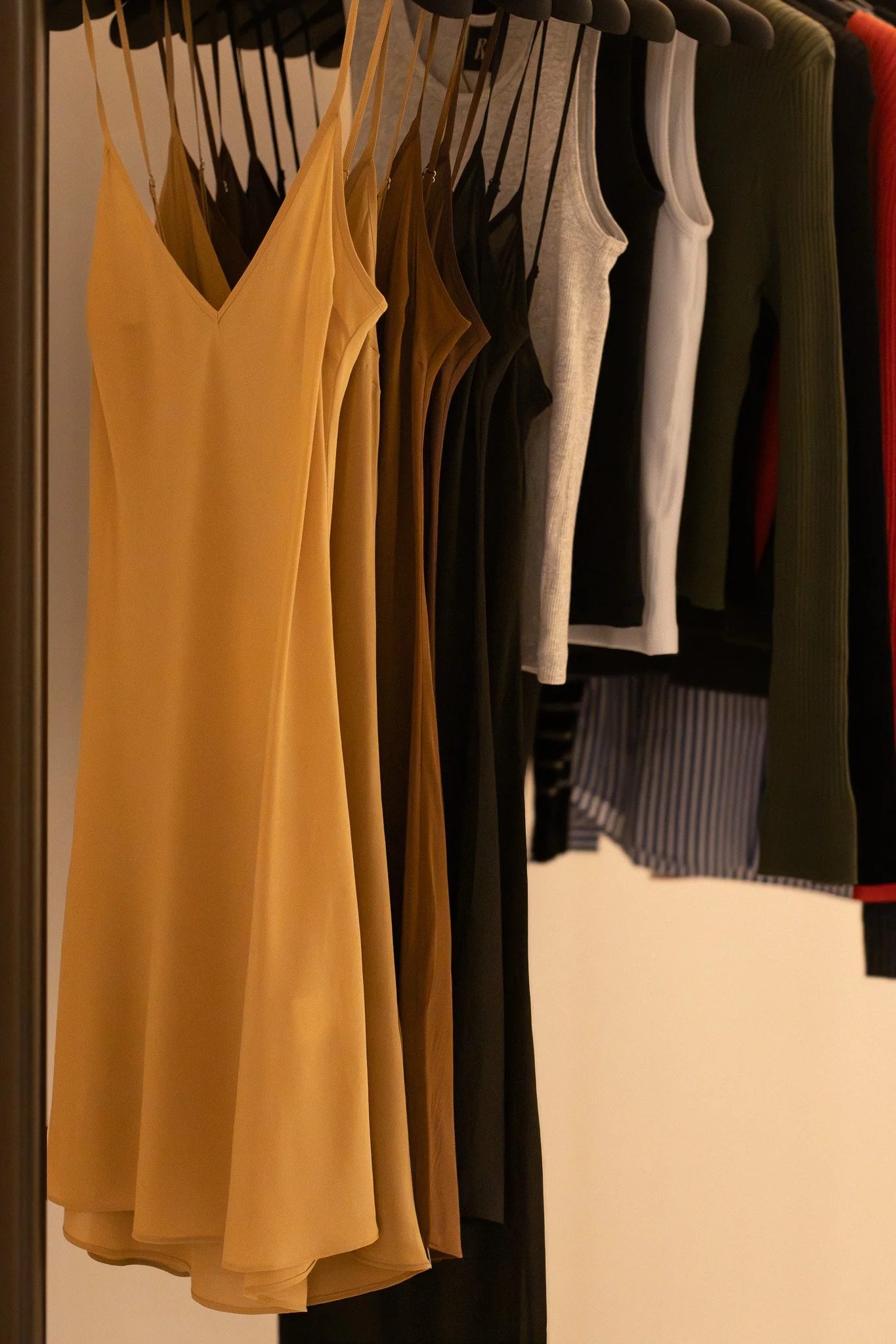 Various clothing items including sleeveless dresses, tank tops, skirts, and striped clothing hanging on a rack in a store. Realisation Par.