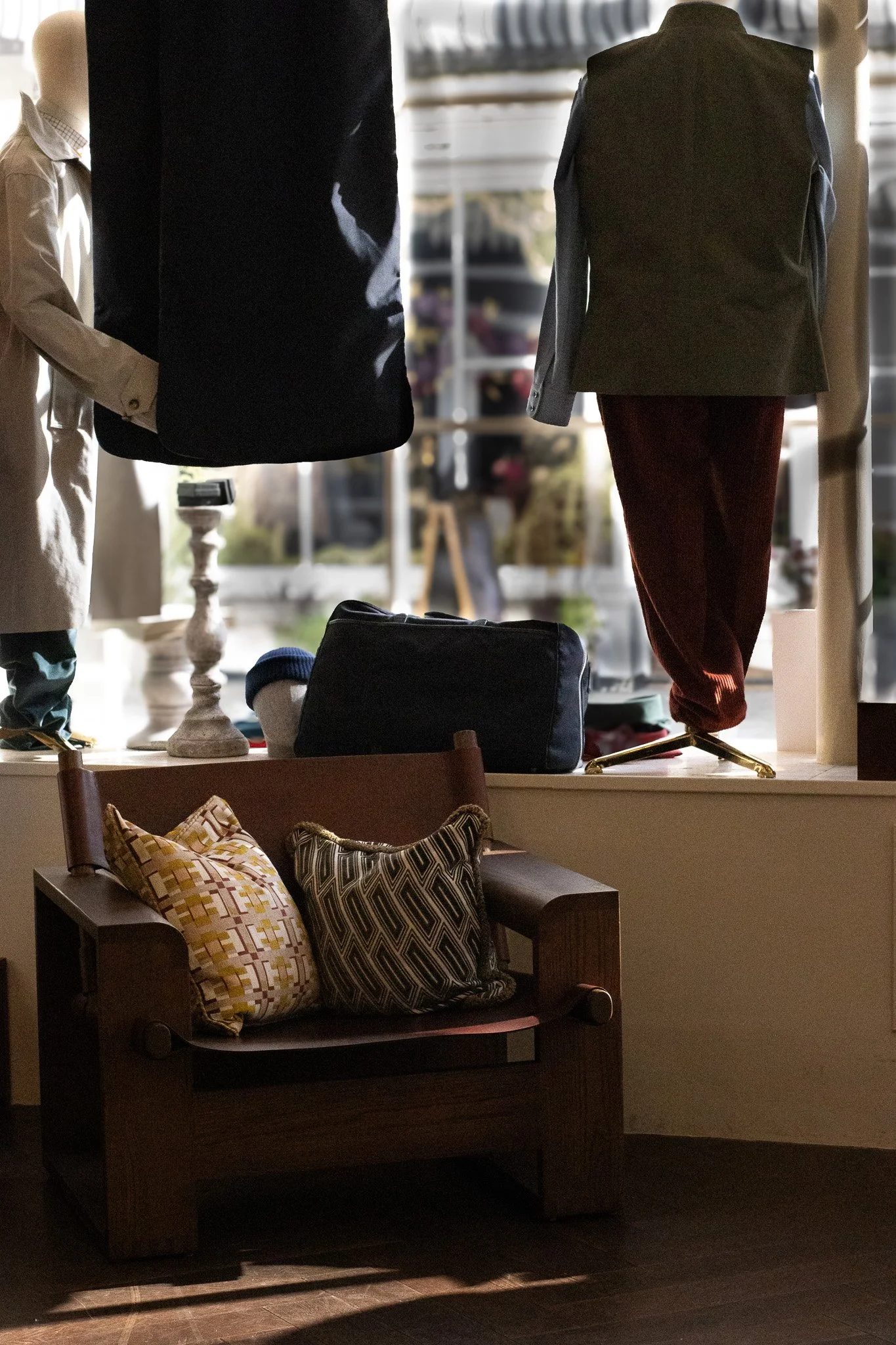 Display window with mannequins dressed in clothing and accessories in a store, with natural light coming through the window. New & Lingwood.