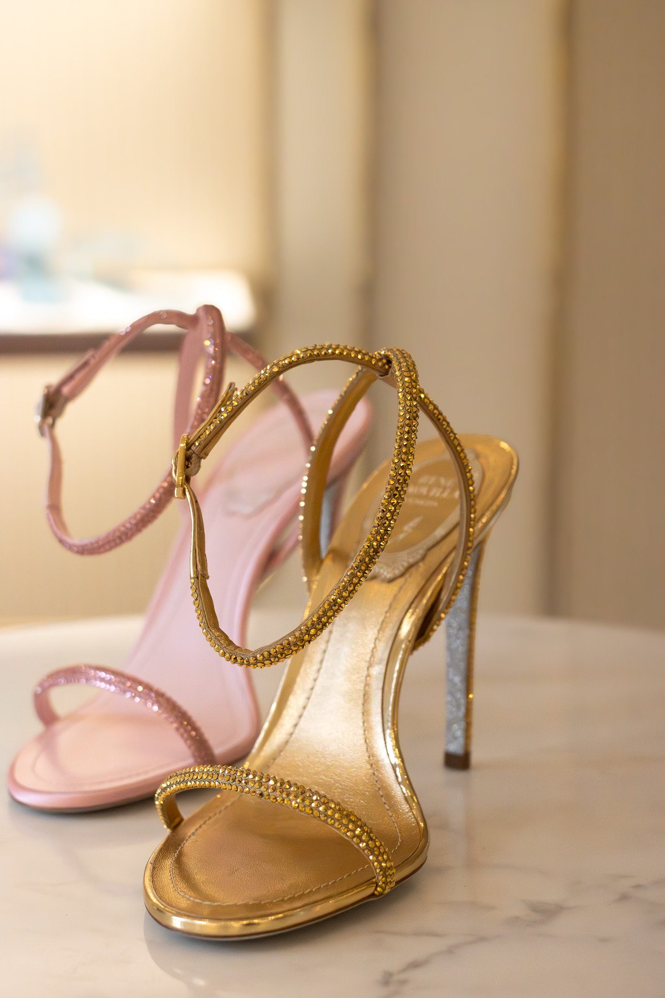 Elegant high-heeled shoes displayed on a stand, with pink and gold colors and rhinestone embellishments. Rene Caovilla.