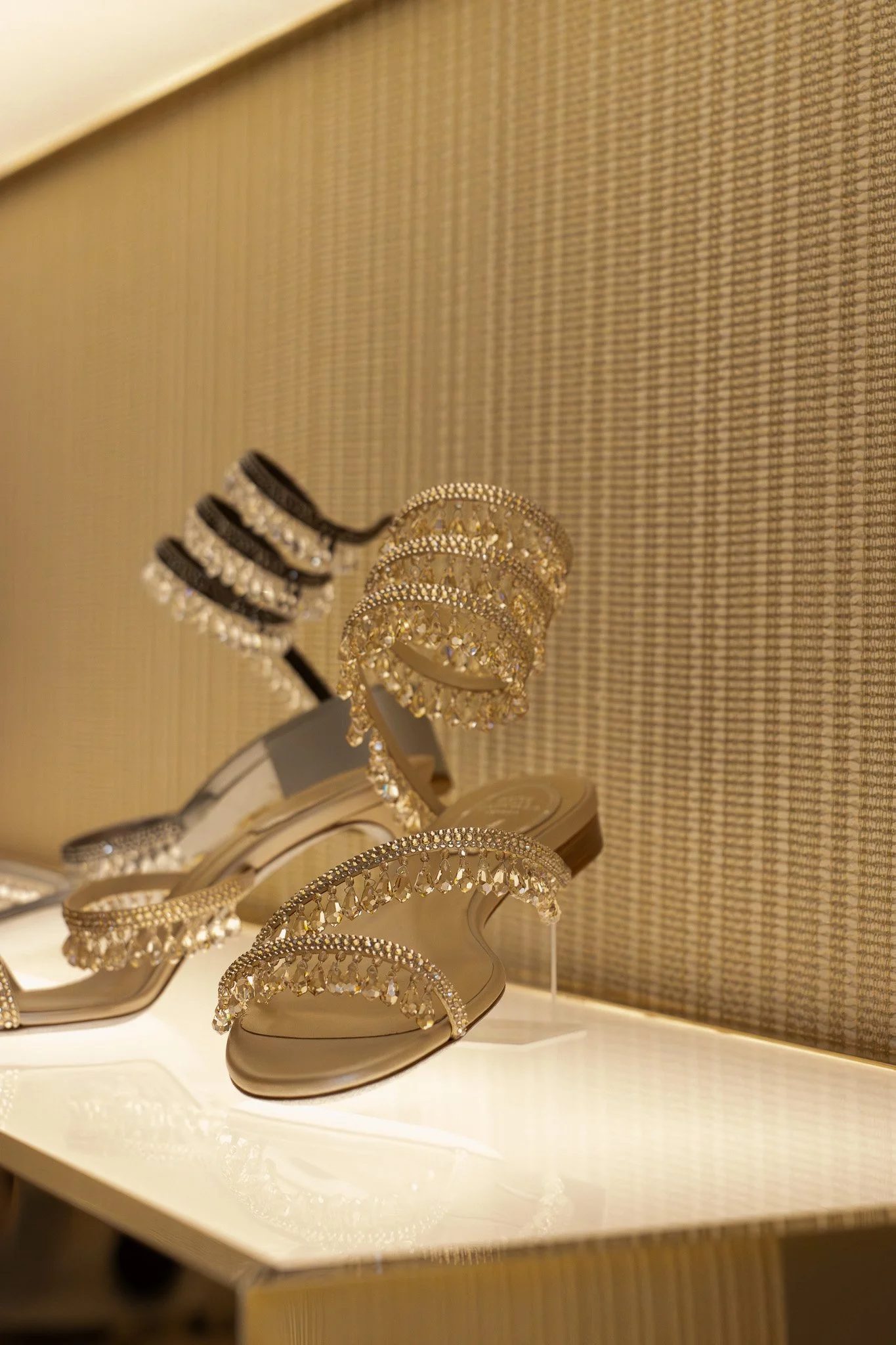 Multiple gold and silver tiaras decorated with rhinestones displayed on a white shelf. Rene Caovilla.