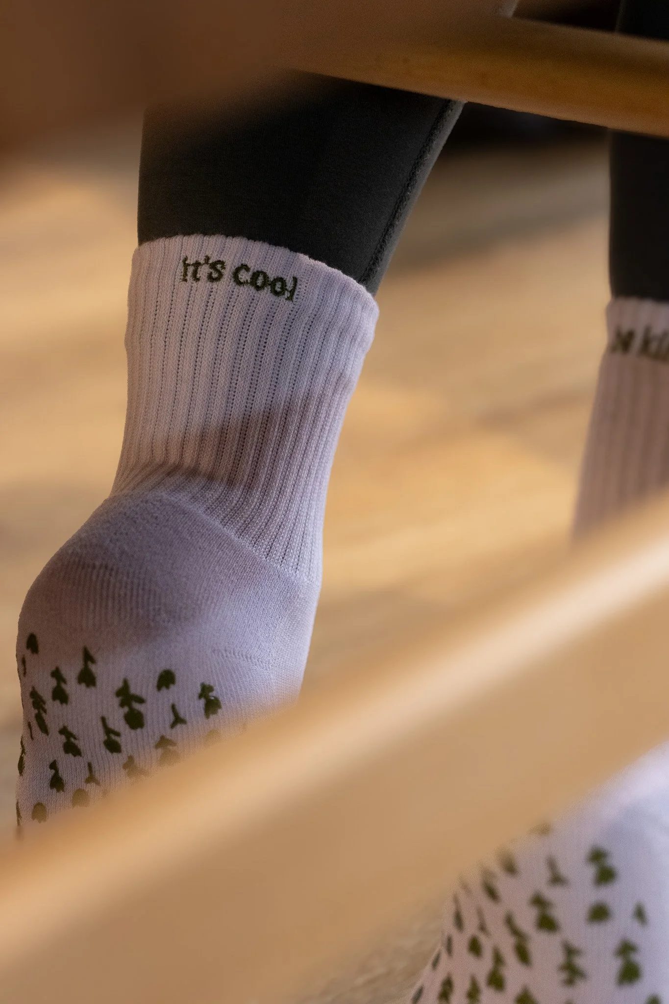 Close-up of a person's white sock with the words 'It's cool' embroidered near the top, and small black tree patterns near the toe area, partially visible. GetAGrip Apparel.