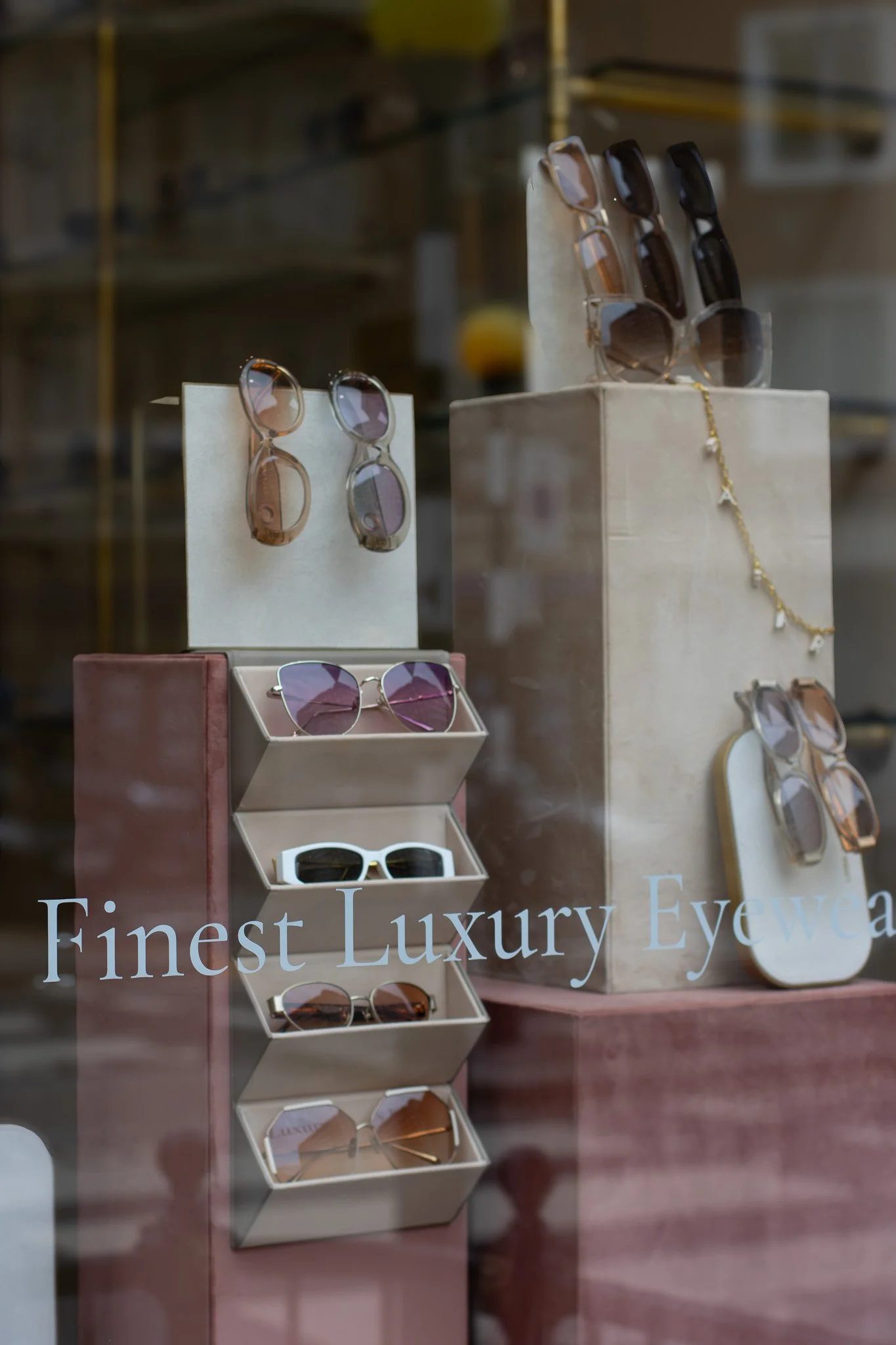 Display window with various sunglasses and eyewear on mannequins and stands, with the words "Finest Luxury Eyewear" visible on the window. Linda Farrow.