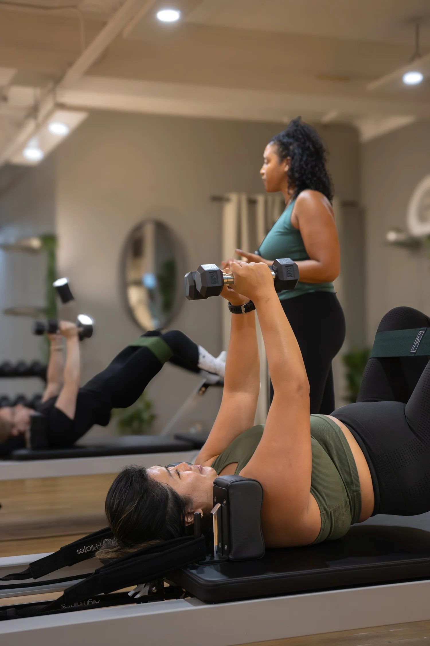 Women performing leg exercises with dumbbells on a reformer machine in a fitness class. The Studio Cheltenham, Reformer Pilates.