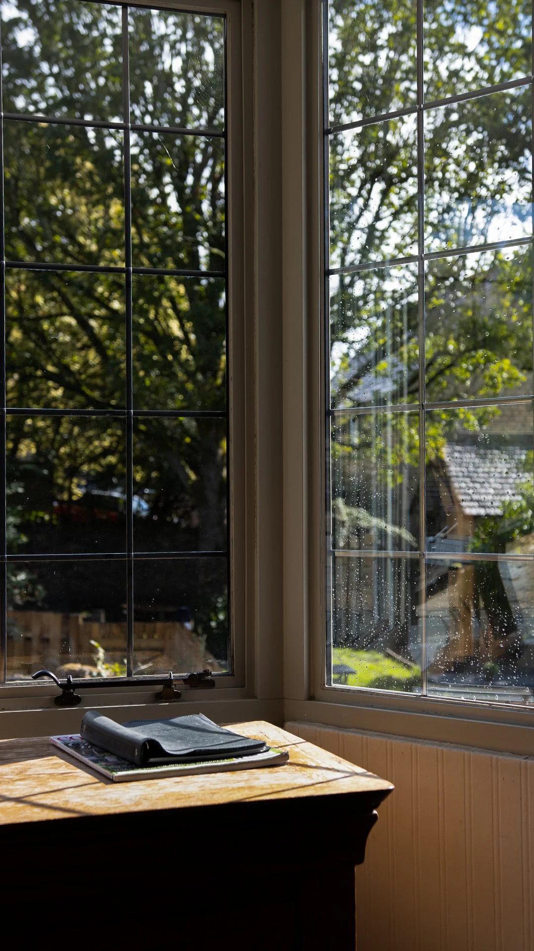 View from inside a room looking out two open windows at a trees and a house outside during daytime. The Lamb Inn.